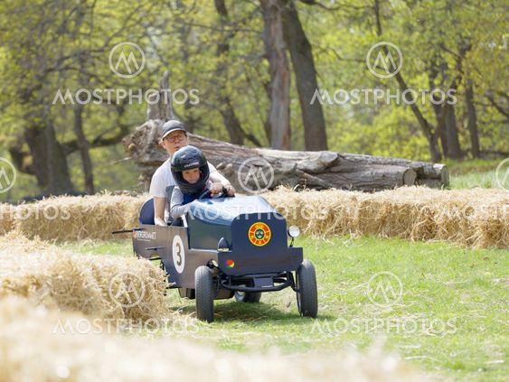 Smiling boy and mother driving a green soapbox car...
