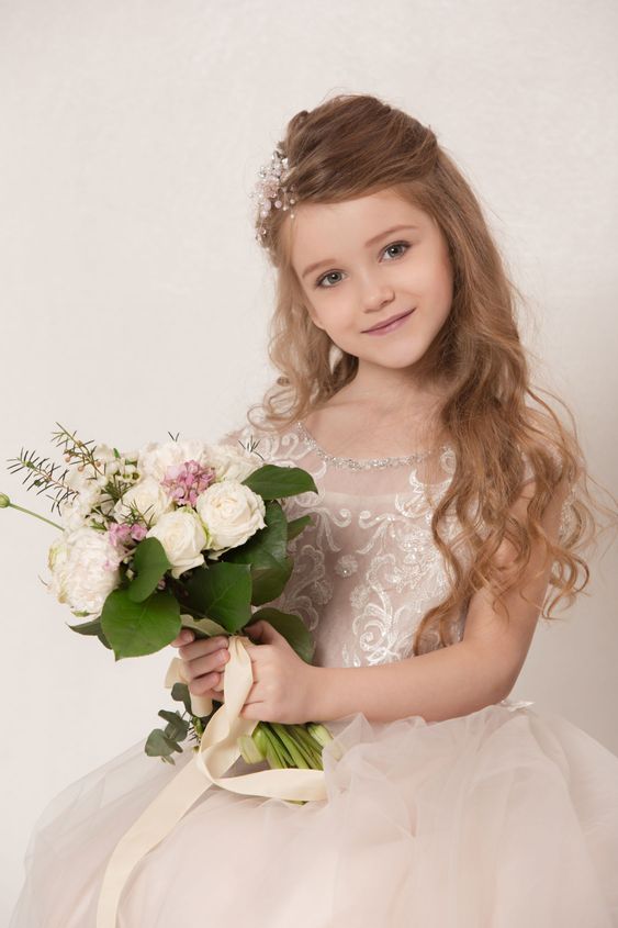 Little pretty girl with flowers dressed in wedding dresses