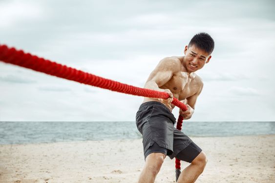 Young healthy man athlete doing squats at the beach