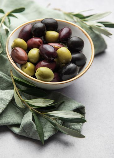 Colorful olives are served in a bowl with olive branches