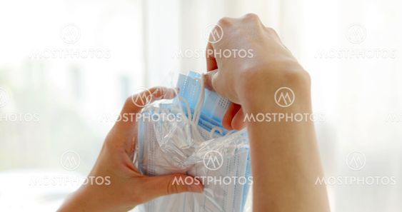 Crop woman taking out medical face mask from package in...