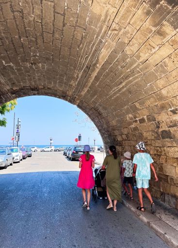 Family walking through stone archway towards seaside...