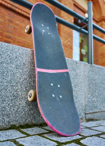 Used pink skateboard against stone wall in urban setting