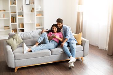 Hindu couple cuddling on couch looking at phone together