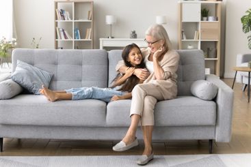 Little girl relax on couch in caring embraces of grandma