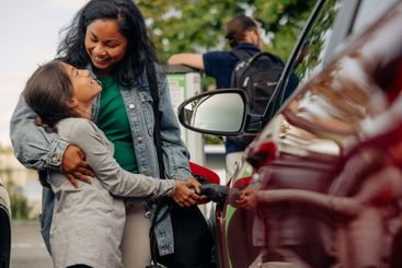 Happy woman embracing daughter while charging electric...
