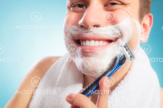 Happy man shaving using razor with cream foam.