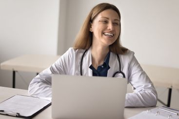 Joyful millennial female doctor sitting by notebook...