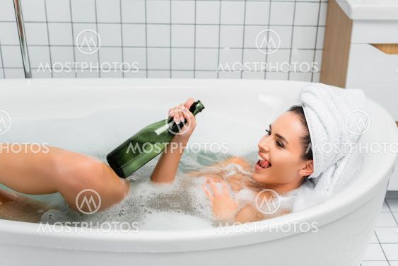 Cheerful woman with towel on head bathing with bottle of...