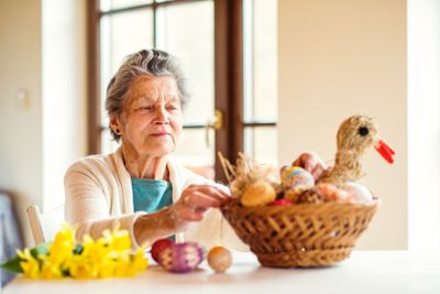 Senior woman arranging basket with Easter eggs and...
