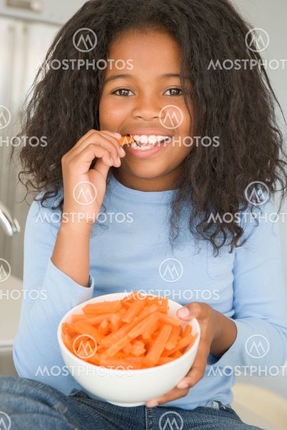 Young girl in kitchen eating carrot sticks smiling