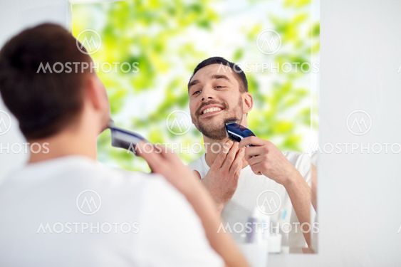 man shaving beard with trimmer at bathroom