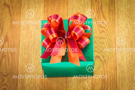Green gift box with red bow on wood
