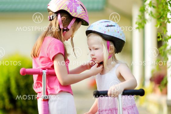 Little girl helping her sister to put a helmet on