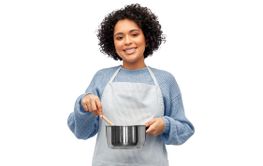 happy woman in apron cooking food in saucepan