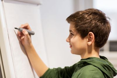student boy with marker writing on flip board