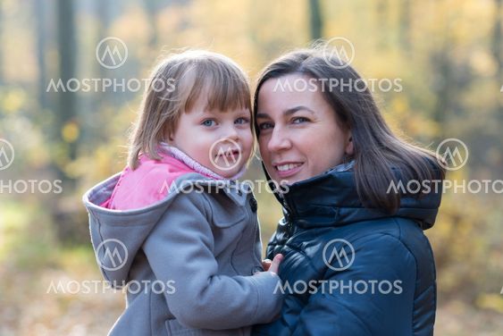 Mother holding daughter in autumnal forest smiling