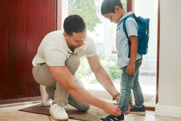 Father, tying shoes and school with son by door for...