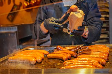 Grilled sausages being prepared on food stand with hands...