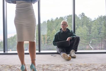 A blonde man sitting casually on the floor of a modern...