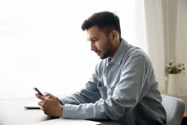 Busy young man sit at desk focused on smartphone screen