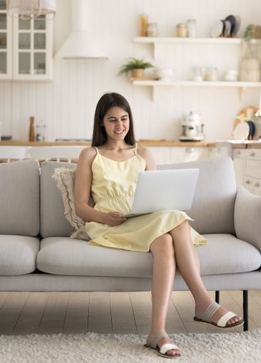 Happy young woman using notebook sitting on sofa at home