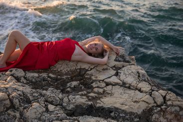 woman in red dress lying on a rock by the sea