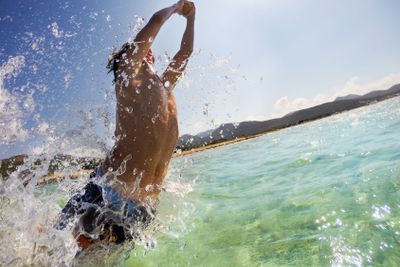 Caucasian young boy jumping in water, playing and having...