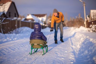Young father sledding his little daughter on a sled in the snow outdoors