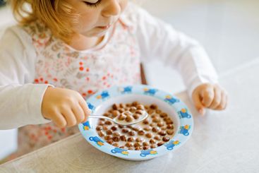 Close up of toddler girl eating healthy cereal with milk...