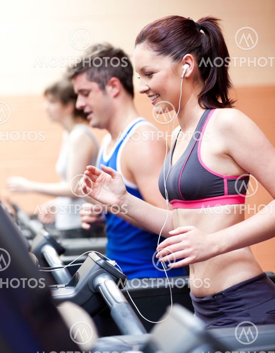 Beautiful female athlete standing on a running machine listening to the music