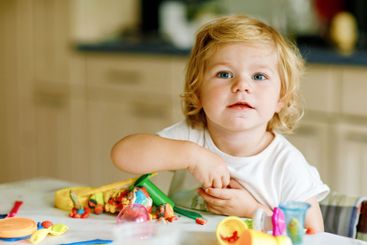 Adorable cute little toddler girl with colorful clay at...