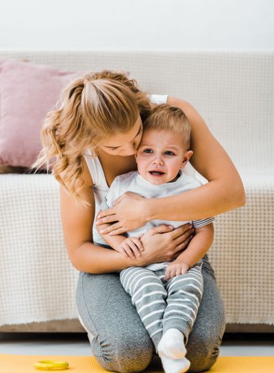 crying toddler boy with mother on carpet near couch