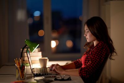 student or woman typing on laptop at night home