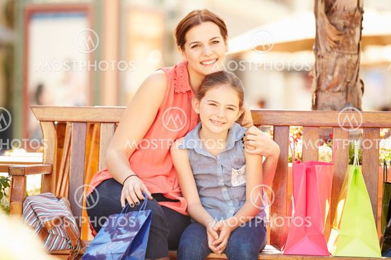Mother And Daughter Sitting On Seat In Mall Together
