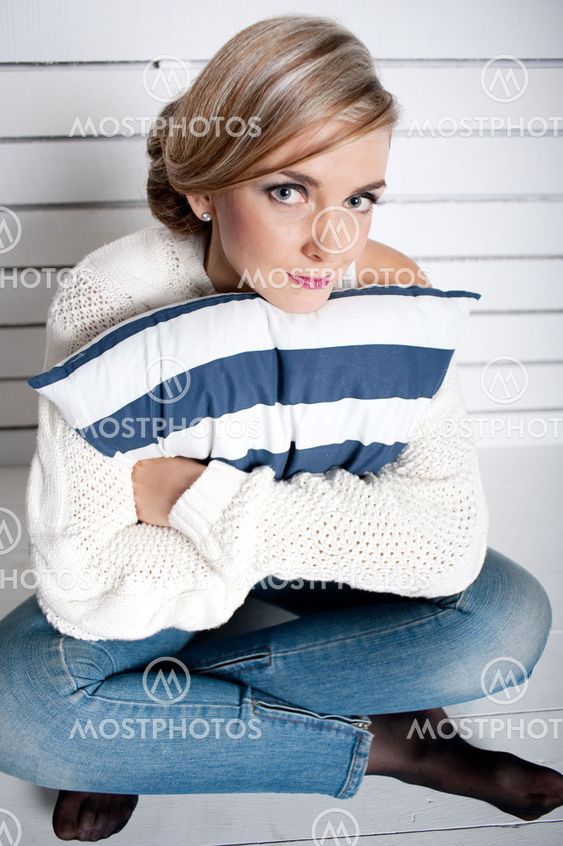 The young girl sits on a floor and embraces a pillow