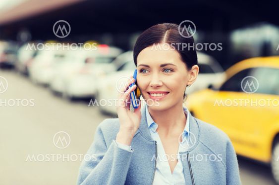 smiling woman with smartphone over taxi in city