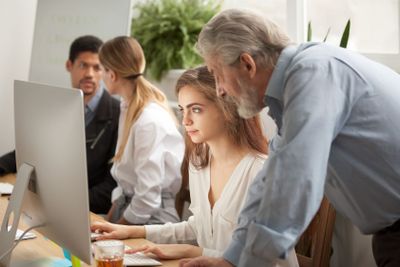 Aged executive manager supervising computer work of...