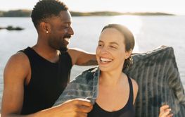 Happy man helping female friend in wrapping towel at sunny day