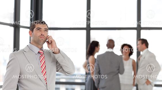Charming businessman holding a phone at workplace with his colleagues