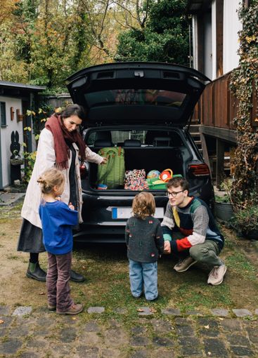 Father and mother talking to children near electric car...