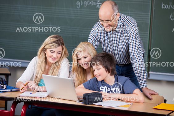 Students Using Laptop While Professor Looking At It At Desk