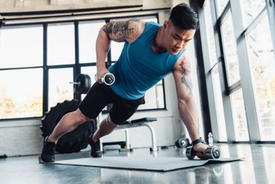concentrated young sportsman exercising with dumbbells in...