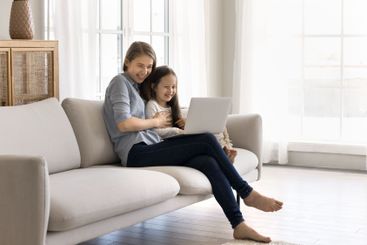 Friendly young mom little daughter using notebook in...