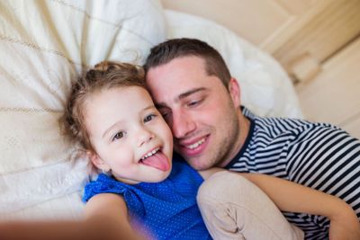 Father and daughter lying in parents bed, taking selfie
