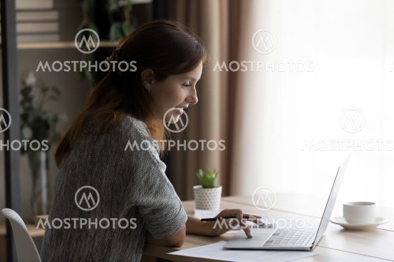 Smiling woman using laptop, working online, sitting at...