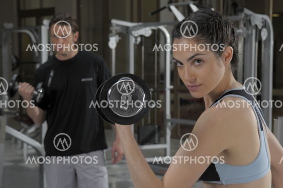 Woman wearing a gray top and black trousers doing weights at gym