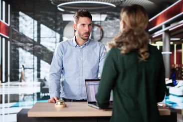 Man At Hotel Talking To Receptionist Woman