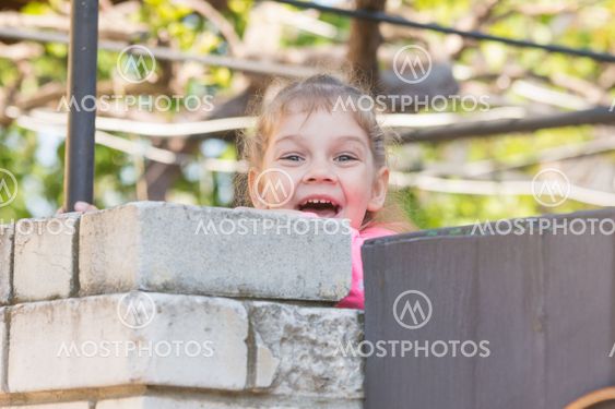 Five-year girl smiling looked out from behind the wall