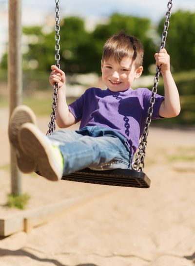 happy little boy swinging on swing at playground